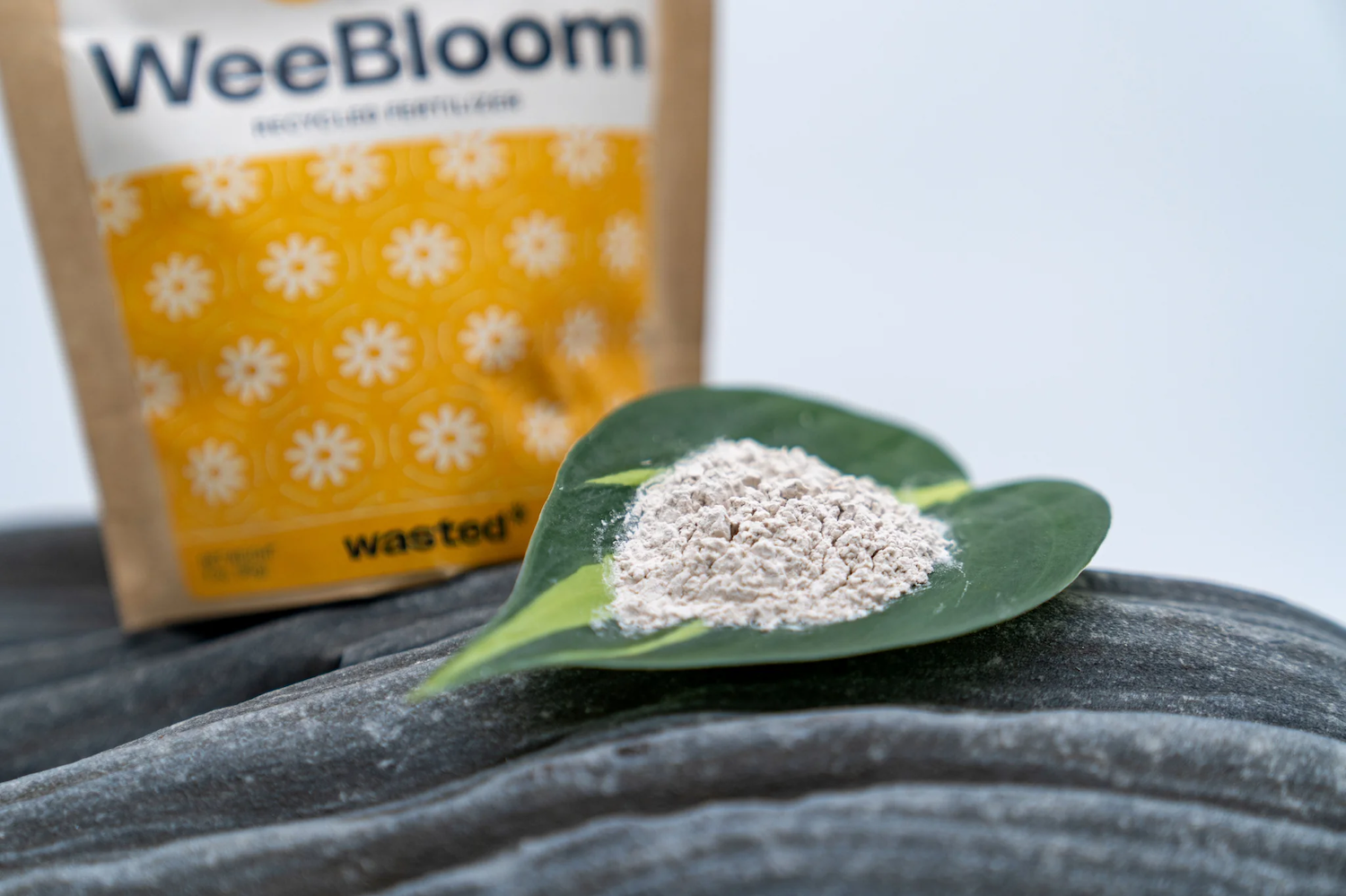 A small pile of WeeBloom fertilizer, a white powder, sits on a leaf.